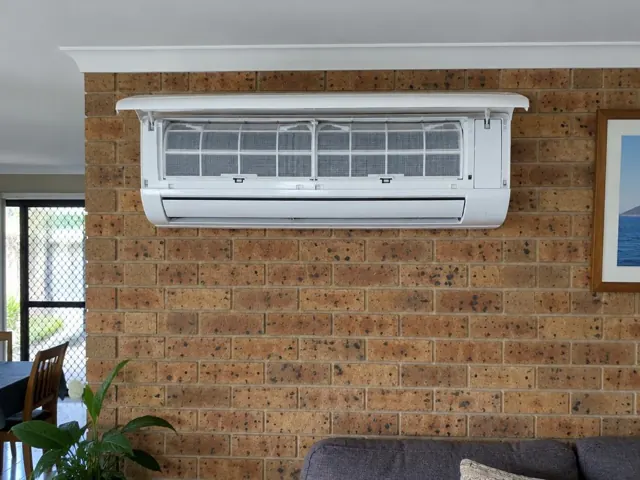 Clean split system with open front panel and visible filters on a brick interior wall in Oxenford