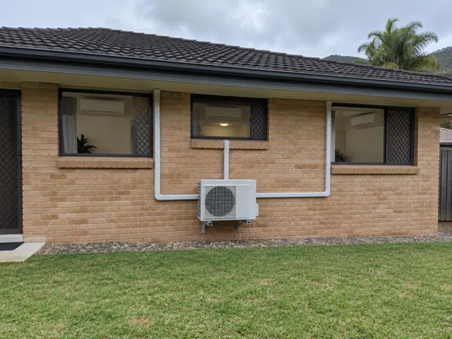 Brick home exterior with three wall-mounted indoor units and one outdoor condenser with pipe covers in Pacific Pines